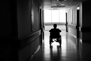 Black and white photo of a man in a wheelchair alone in a hallway