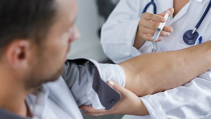 A doctor or nurse, holding a syringe and preparing to give an injection to a male patient.